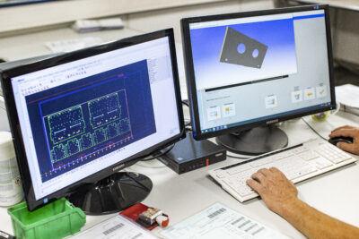 Employee sits in front of two monitors on which CAD designs can be seen