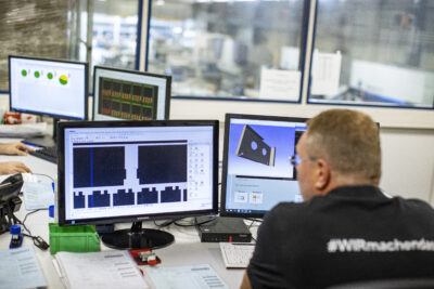 Employee sits in front of two monitors on which CAD designs can be seen